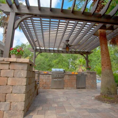 pergola covering an outdoor kitchen with grill built in and stainless steel appliances