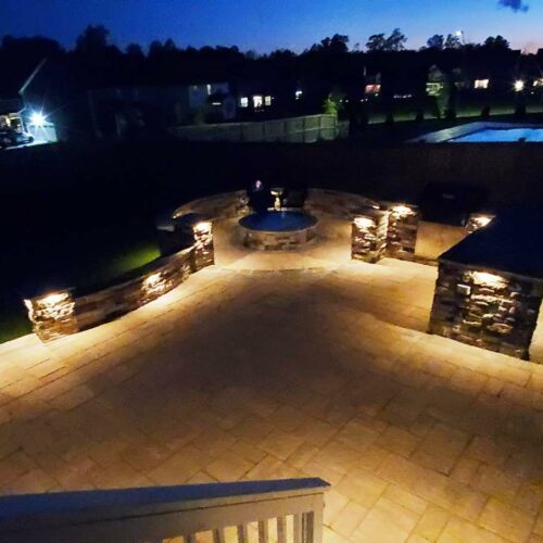 Stone retaining walls, pillars and an island with custom lighting. on a patio paver patio with a custom firepit