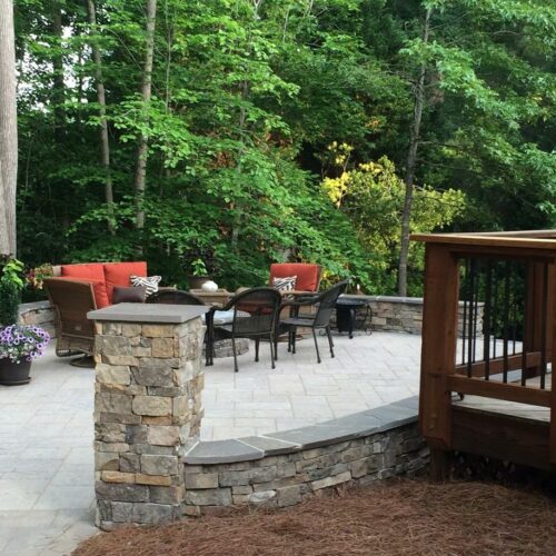 Custom wooden deck that leads out to a custom patio of pavers with retaining walls and columns