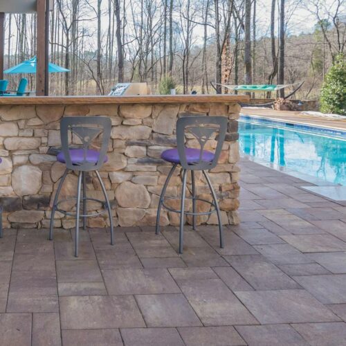 Custom pool deck with outdoor kitchen and island top with stools around it