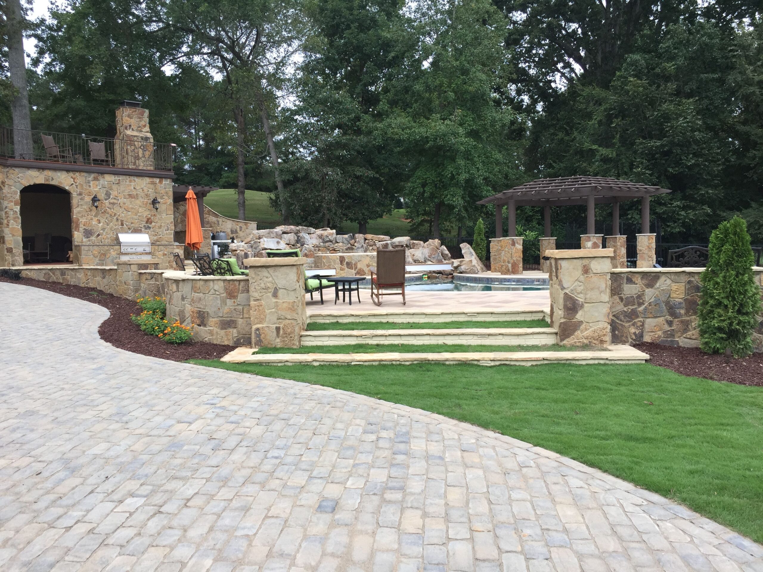 Outdoor living space with stone fireplace, outdoor kitchen, retaining wall and custom paver patio pool deck